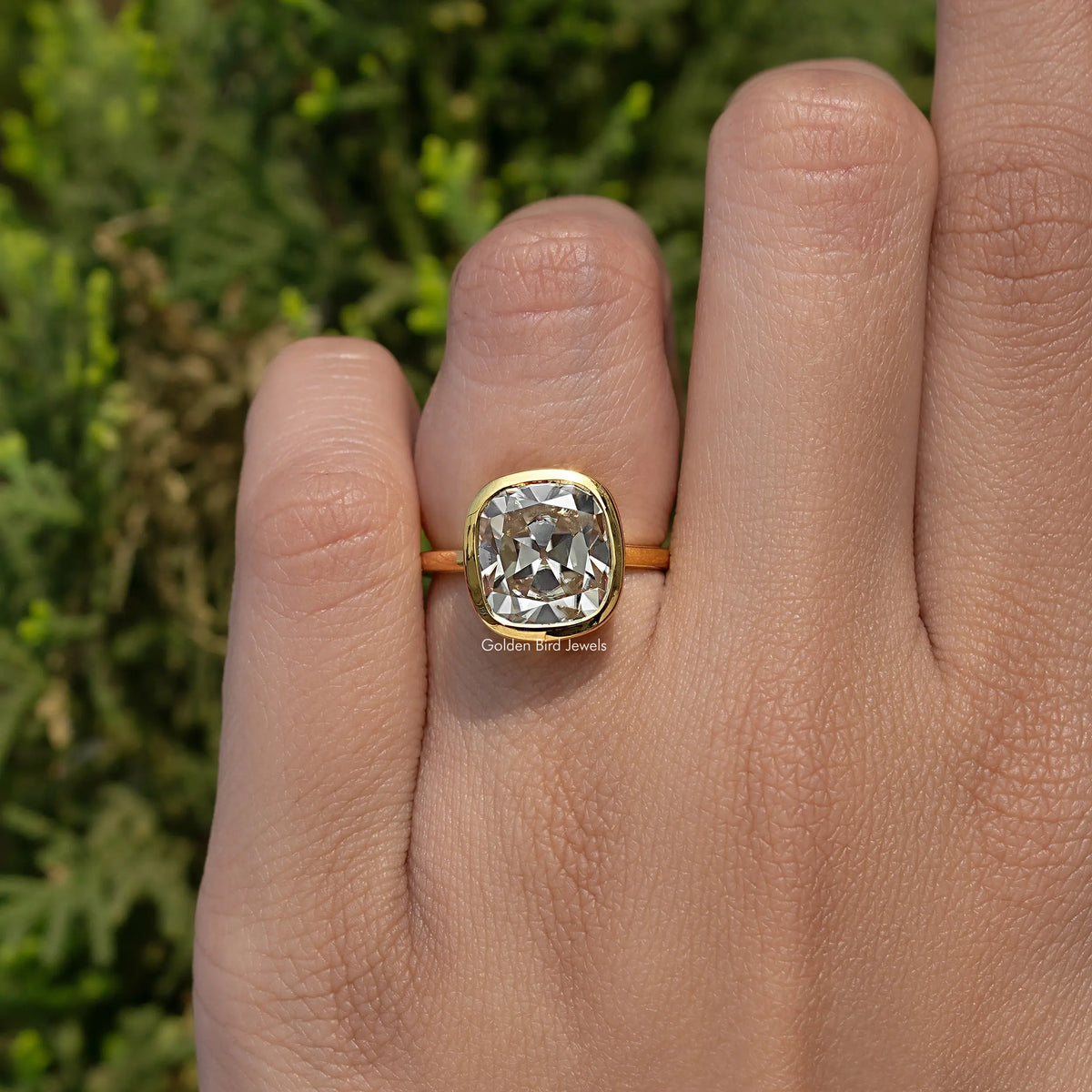 Cushion-cut moissanite bezel engagement ring with gold-tone band on hand