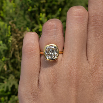 Cushion-cut moissanite bezel engagement ring with gold-tone band on hand
