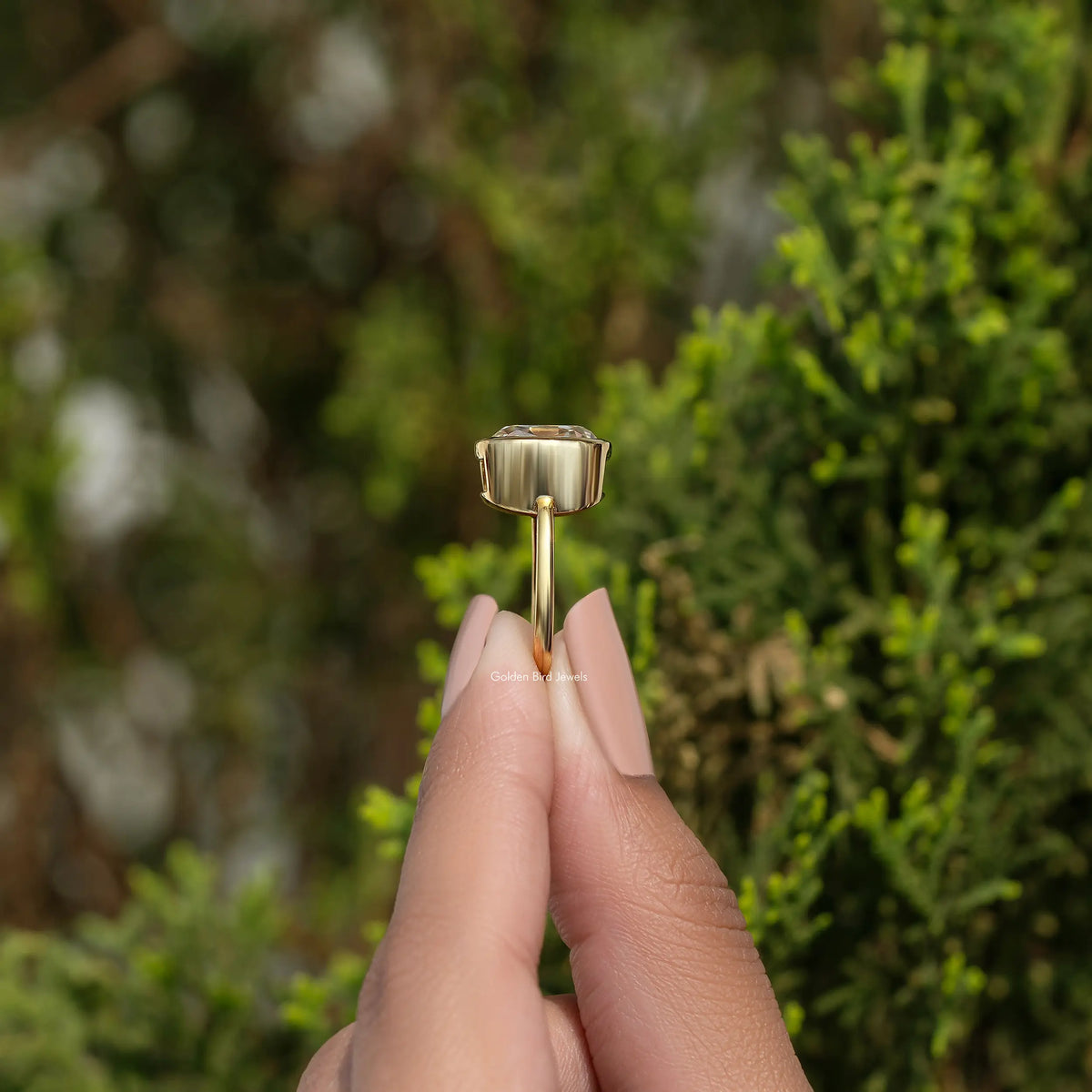 Moissanite bezel engagement ring with gold-tone setting, side profile between fingers