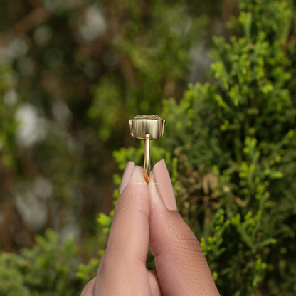 Moissanite bezel engagement ring with gold-tone setting, side profile between fingers