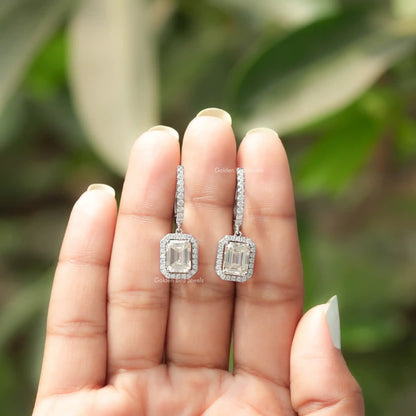 Pair of silver emerald-cut halo drop earrings shown in open hands