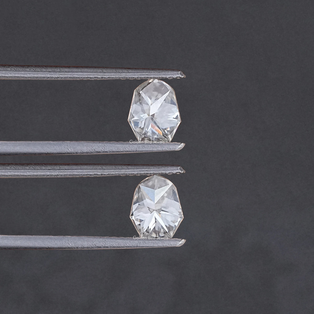 Two shield-cut moissanite stones shown in metal prongs, angled close view