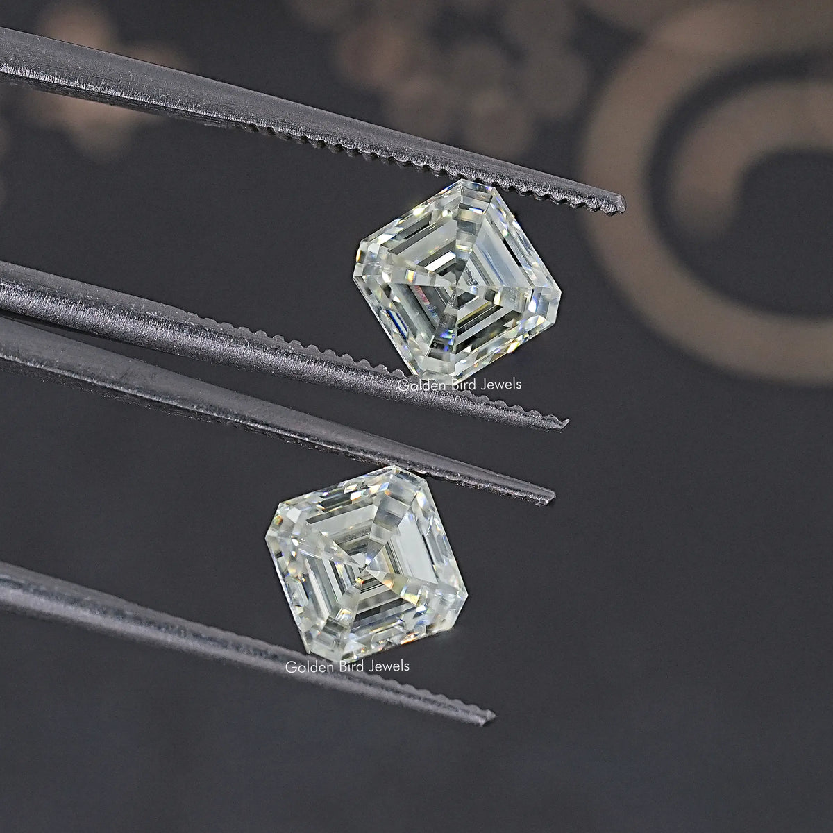 Two clear Asscher-cut moissanite stones held by metal prongs, matching pair