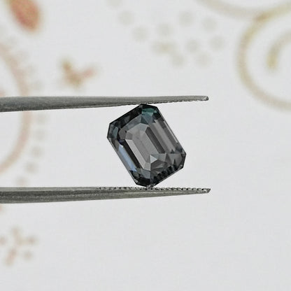Gray emerald-cut gemstone close-up in tweezers, step facets visible