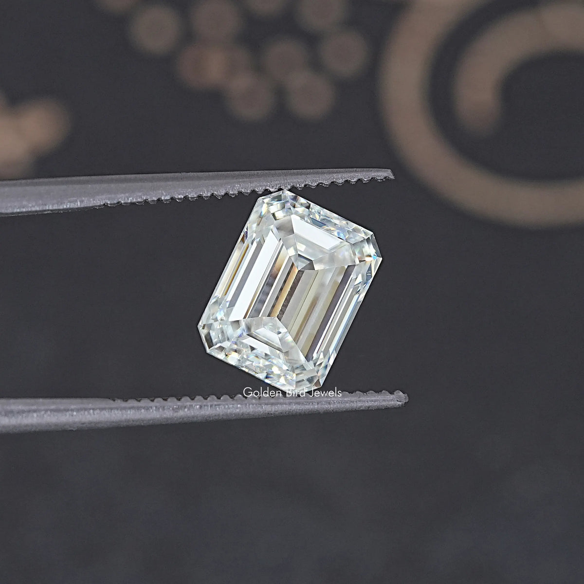 Loose emerald-cut moissanite stone held between tweezers, clear