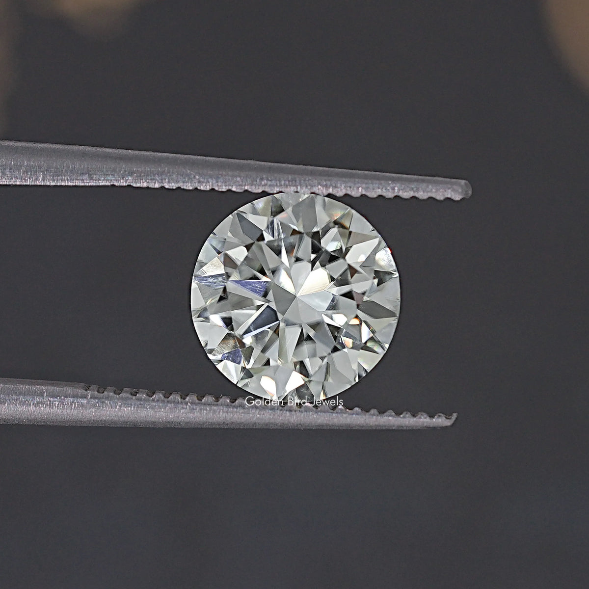 Round moissanite loose stone held by tweezers, close view of faceted sparkle.