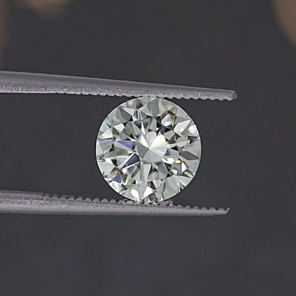 Round moissanite loose stone held by tweezers, close view of faceted sparkle.