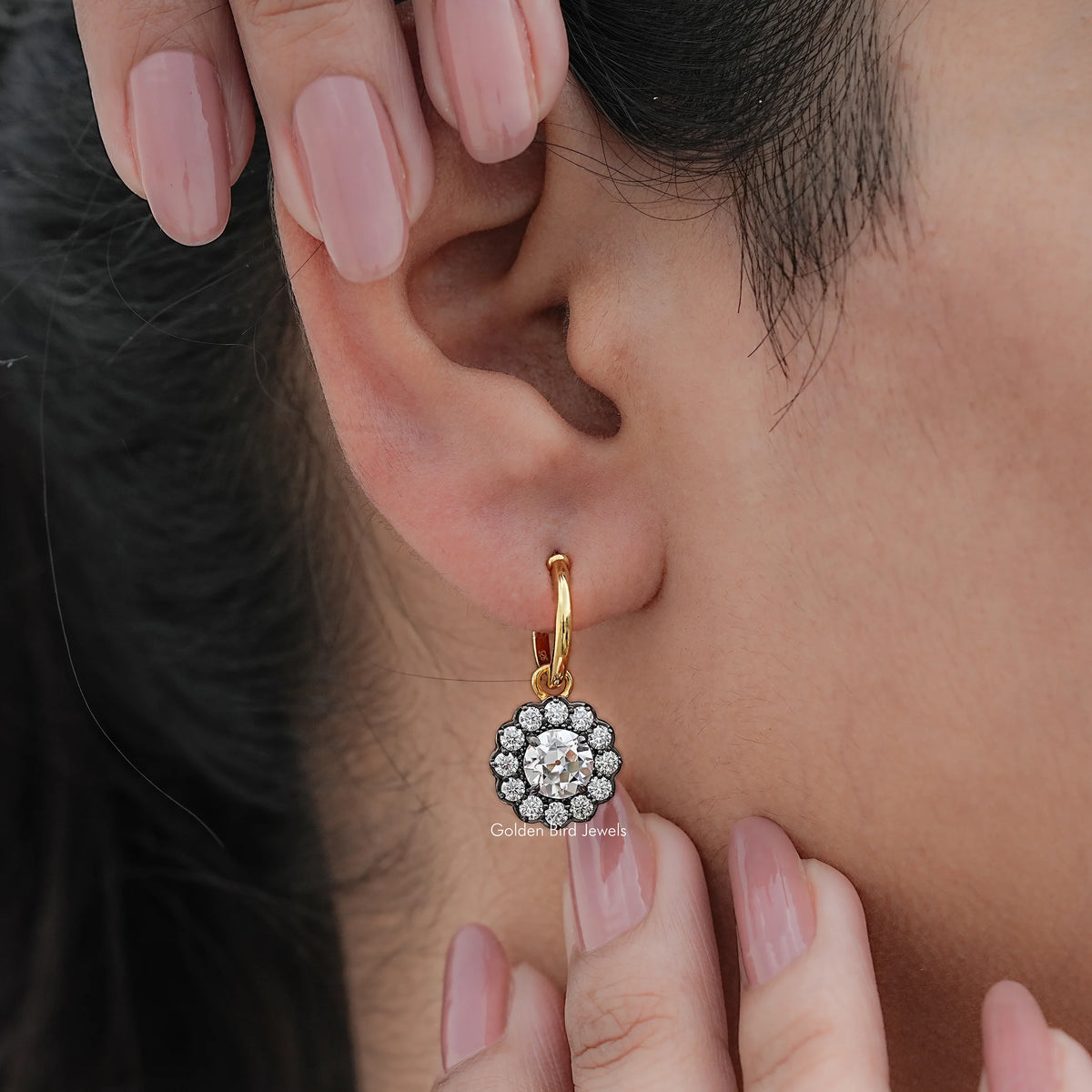 Gold-tone hoop dangle earrings with round clustered halo stones, hands holding near ear