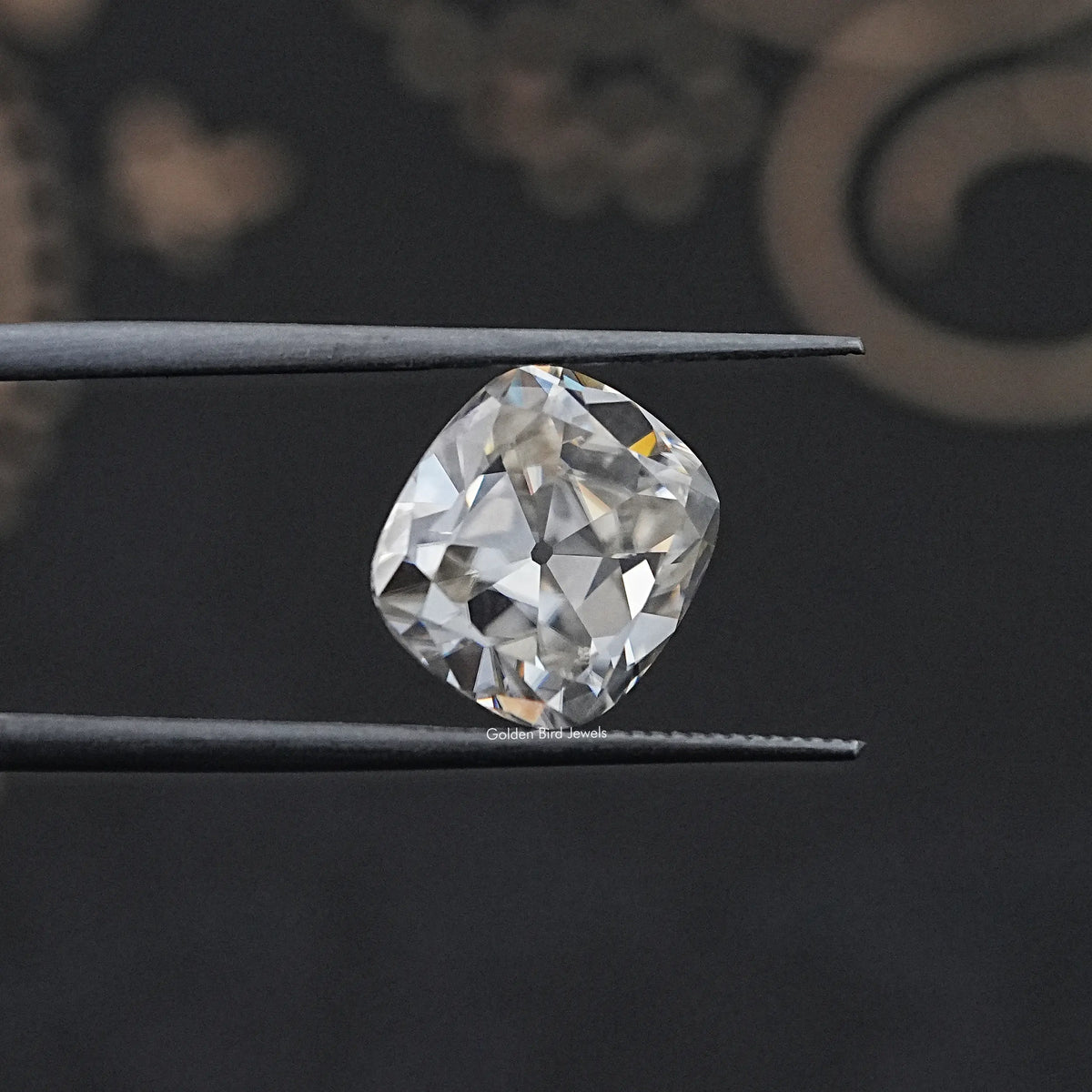 Loose cushion-cut moissanite gemstone held between metal tweezers, white sparkle