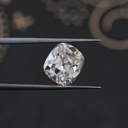 Loose cushion-cut moissanite gemstone held between metal tweezers, white sparkle