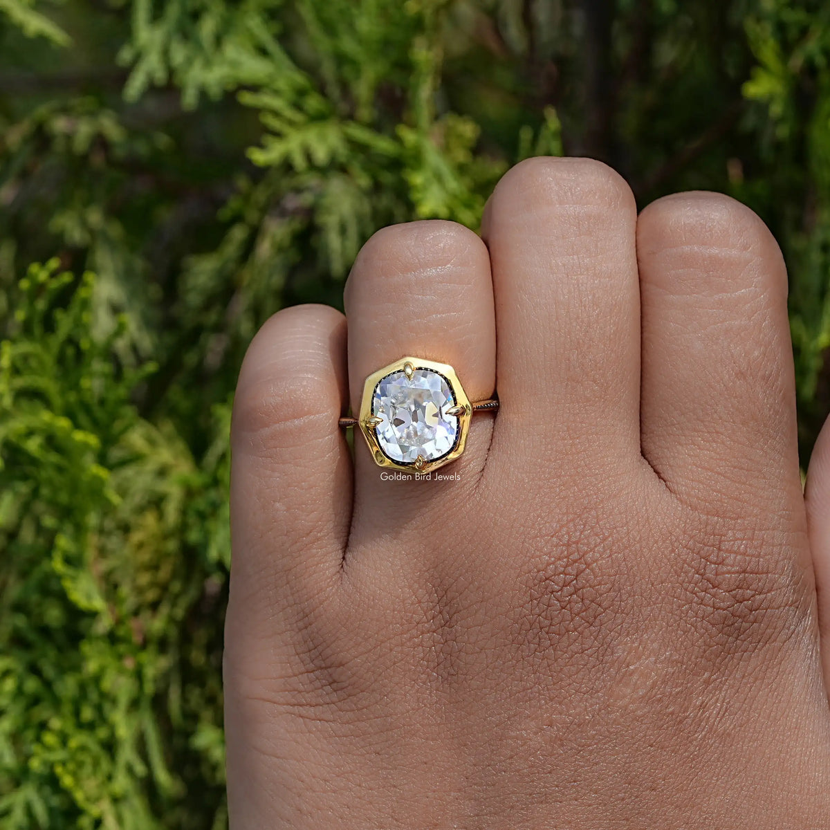 Gold-tone milgrain cushion moissanite engagement ring on palm, square center stone
