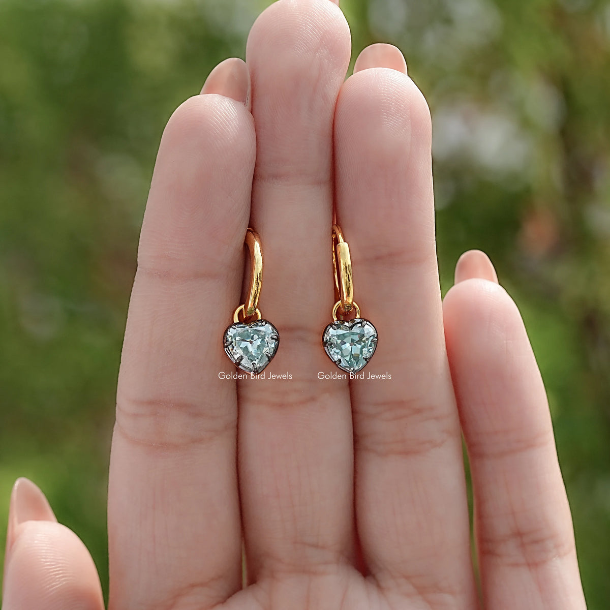 Gold-tone dangle earrings with blue faceted gemstones, shown in hand