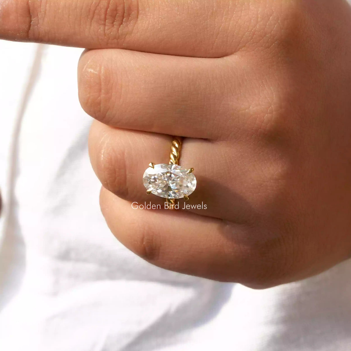 Oval-cut moissanite solitaire ring detail, oval stone and gold-tone 4-prong band