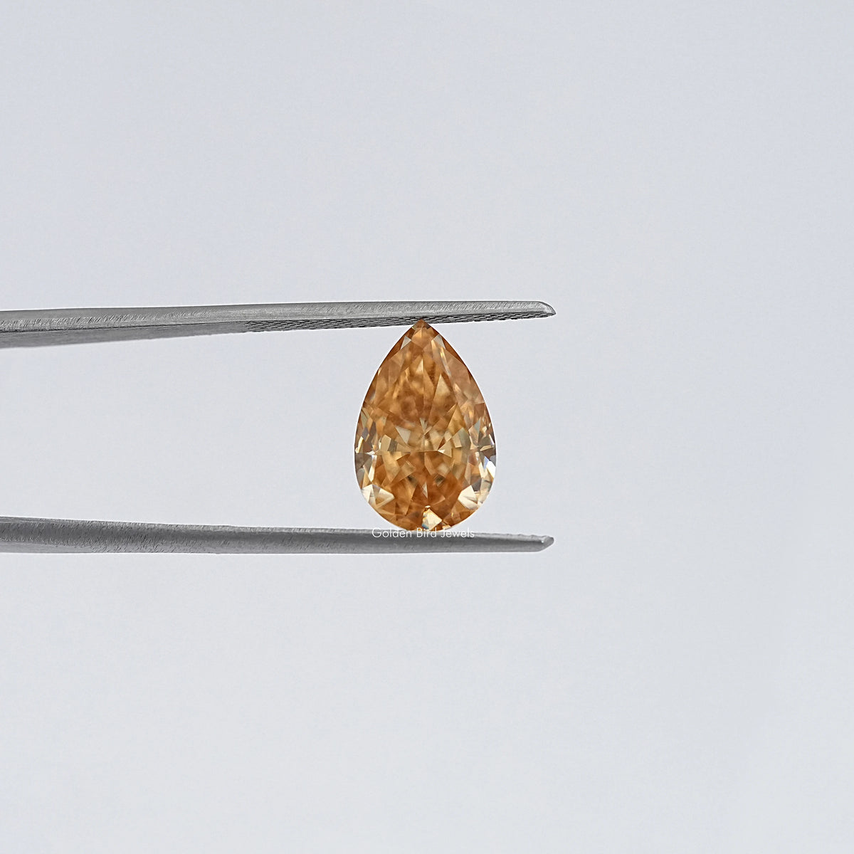 Pear-cut moissanite loose stone in tweezers, honey-gold color, close-up