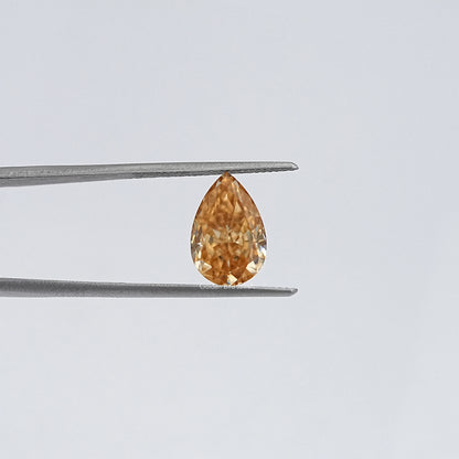 Pear-cut moissanite loose stone in tweezers, honey-gold color, close-up