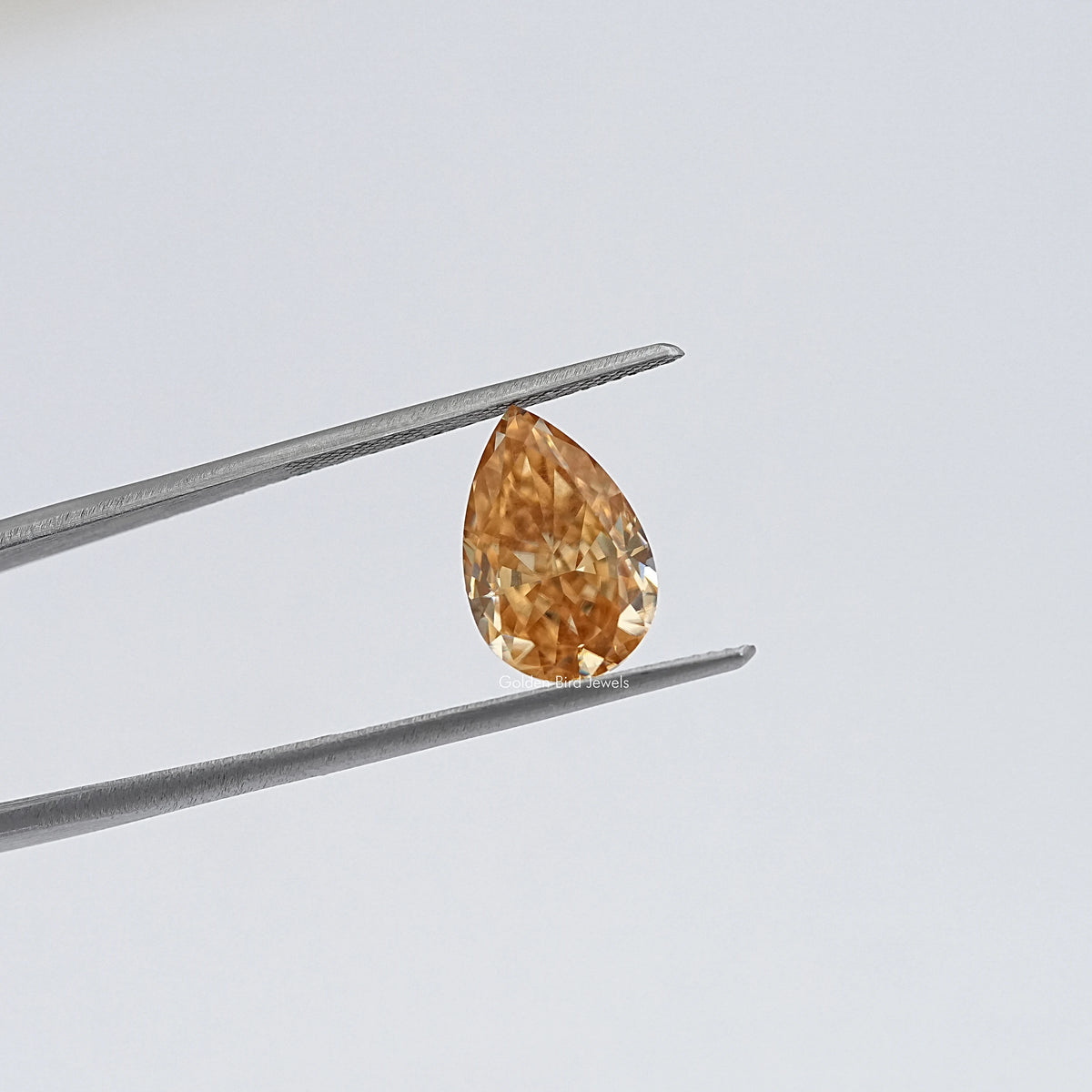 Pear-cut moissanite loose stone in tweezers, warm golden hue, close-up