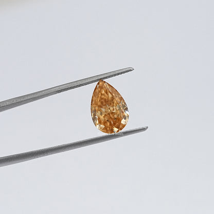 Pear-cut moissanite loose stone in tweezers, warm golden hue, close-up