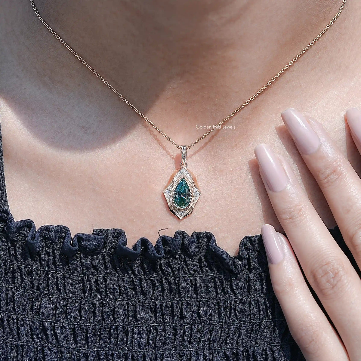 Teal pear-cut pendant with halo accents on a delicate chain, close view