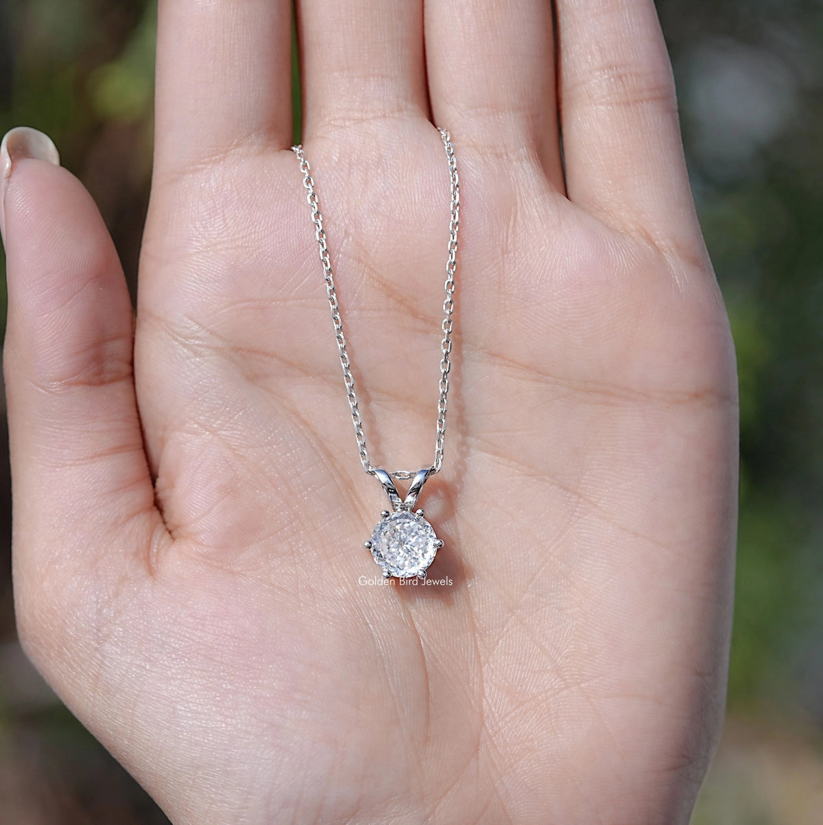 Silver moissanite pendant necklace held in hand, round stone on fine chain