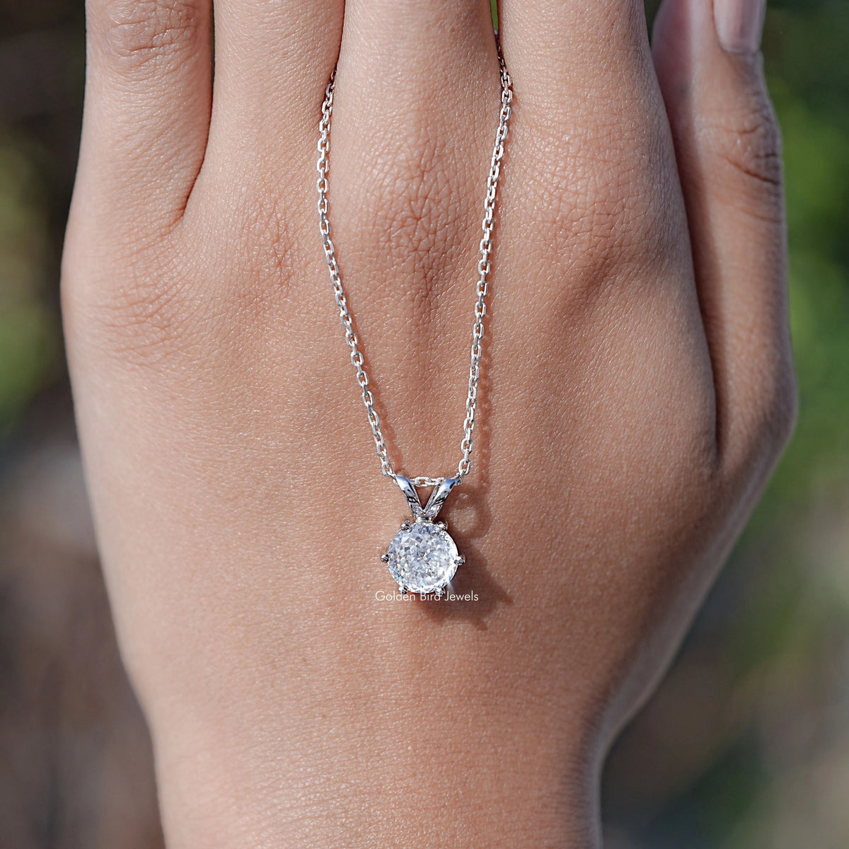 Silver round moissanite pendant necklace on chain, centered over palm view