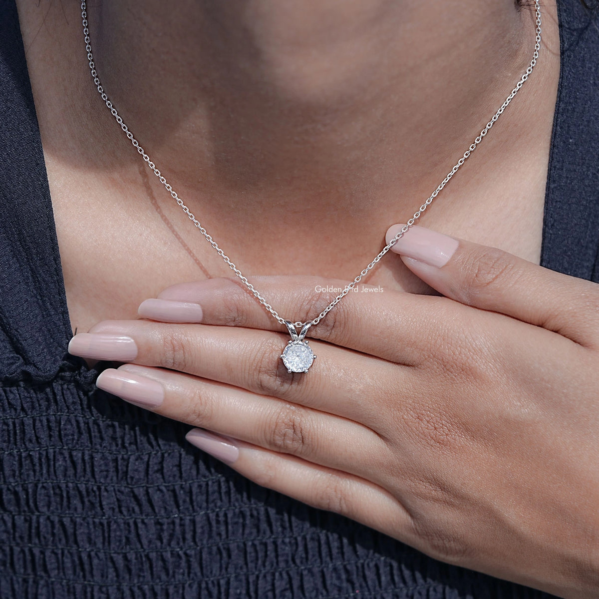 Silver round moissanite pendant on chain resting on neckline, prong-set stone