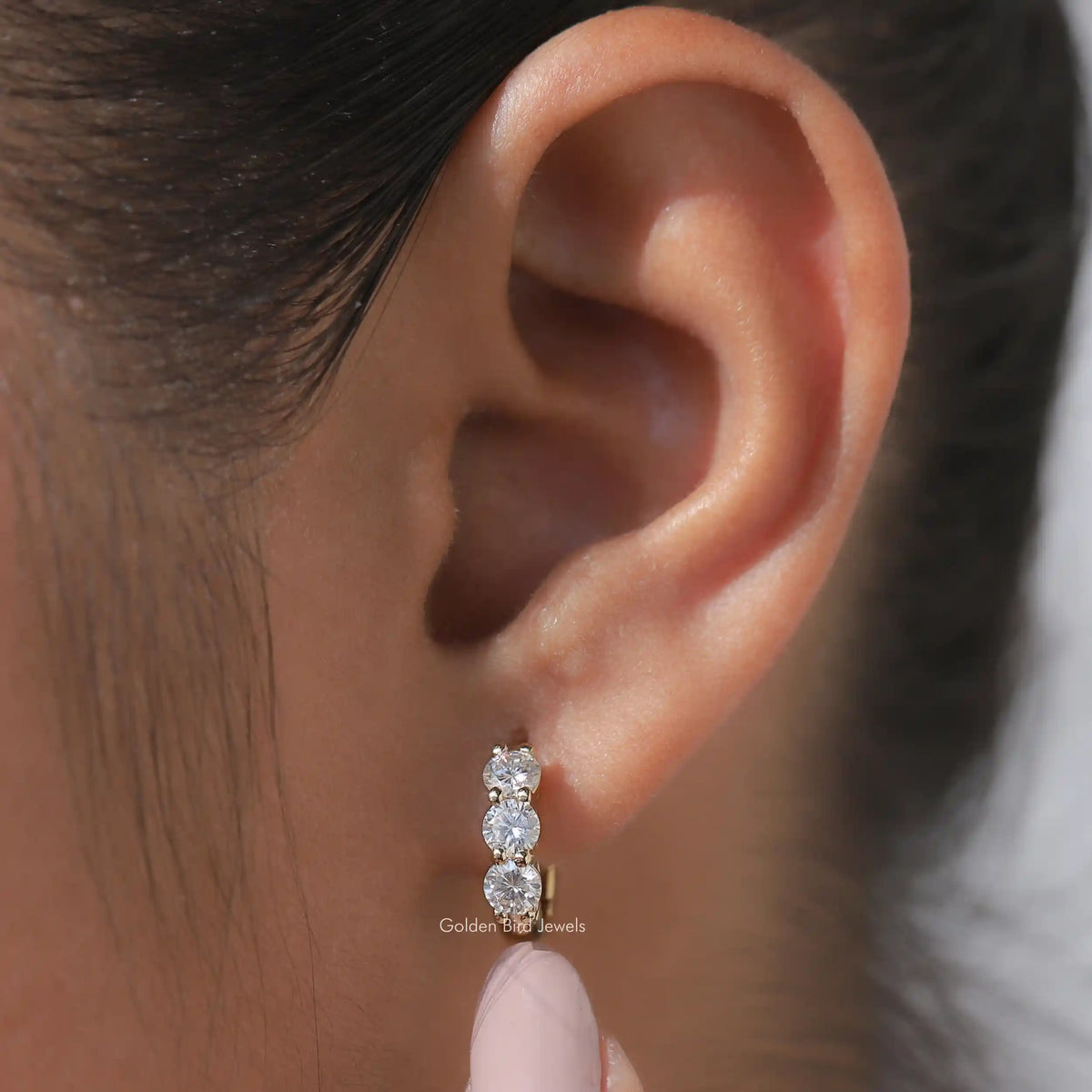 Silver-tone huggie hoop earrings with three round-cut sparkling stones on the ear