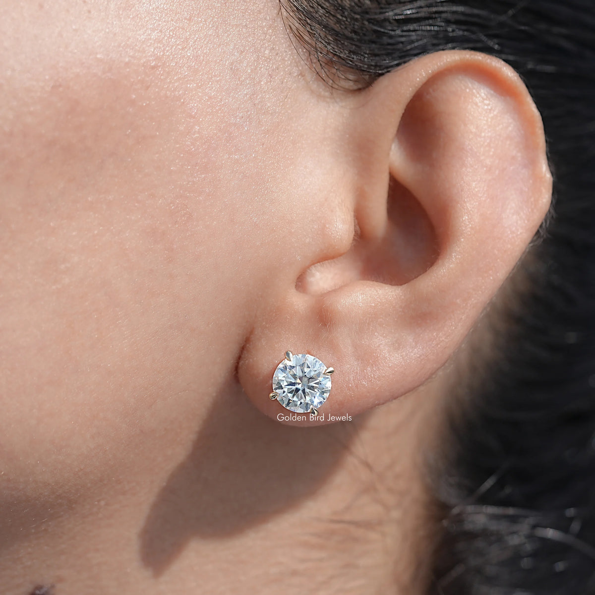 Round moissanite stud earring on ear with gold-tone bezel setting