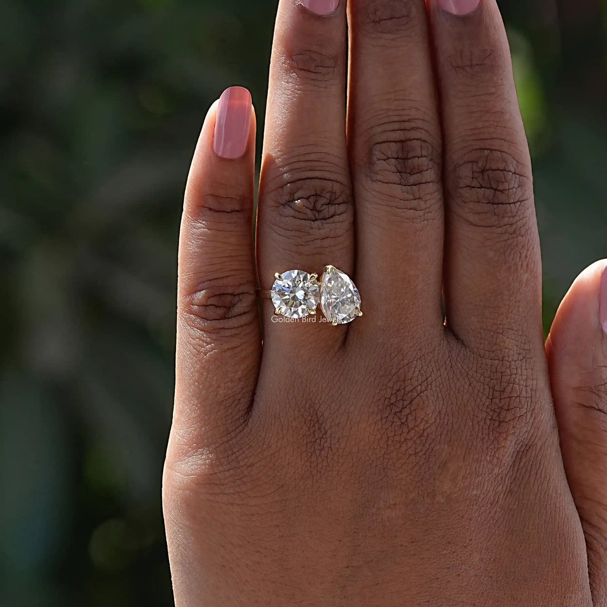 Two-stone toi et moi moissanite ring with round and pear stones on finger