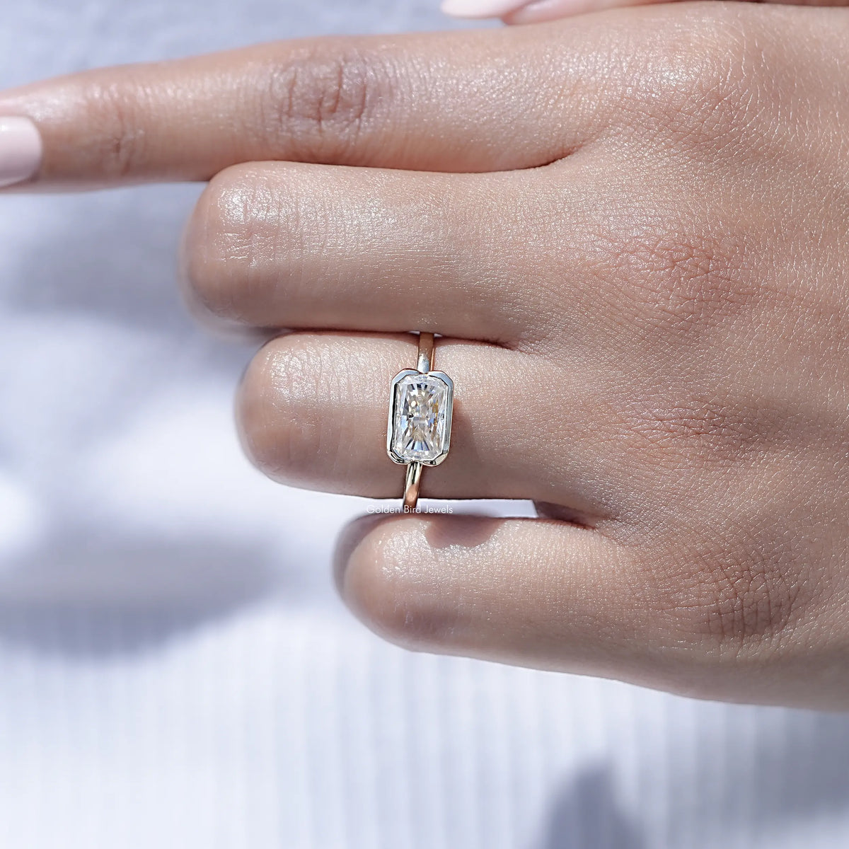 Radiant-cut moissanite solitaire ring on finger with half bezel and thin band