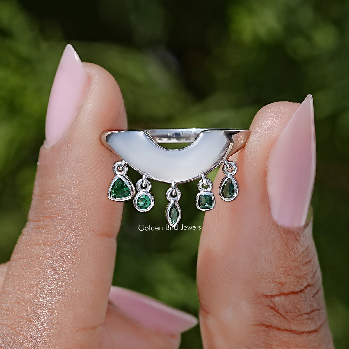 Curved bezel-set engagement ring with green oval and round gemstones, silver band