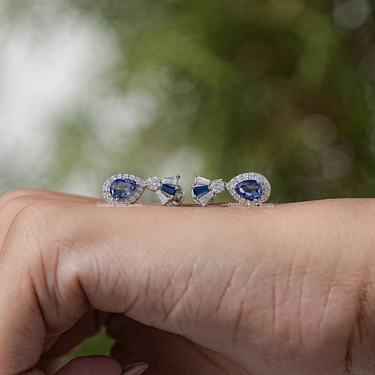 Blue gemstone halo dangle earrings with diamond details, shown resting on palm