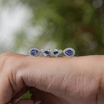 Blue gemstone halo dangle earrings with diamond details, shown resting on palm