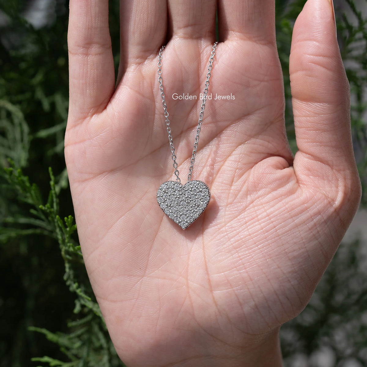 Heart pendant necklace held in hand, silver-tone chain and glittery setting