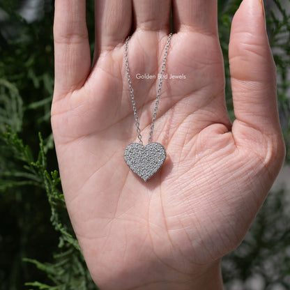 Heart pendant necklace held in hand, silver-tone chain and glittery setting