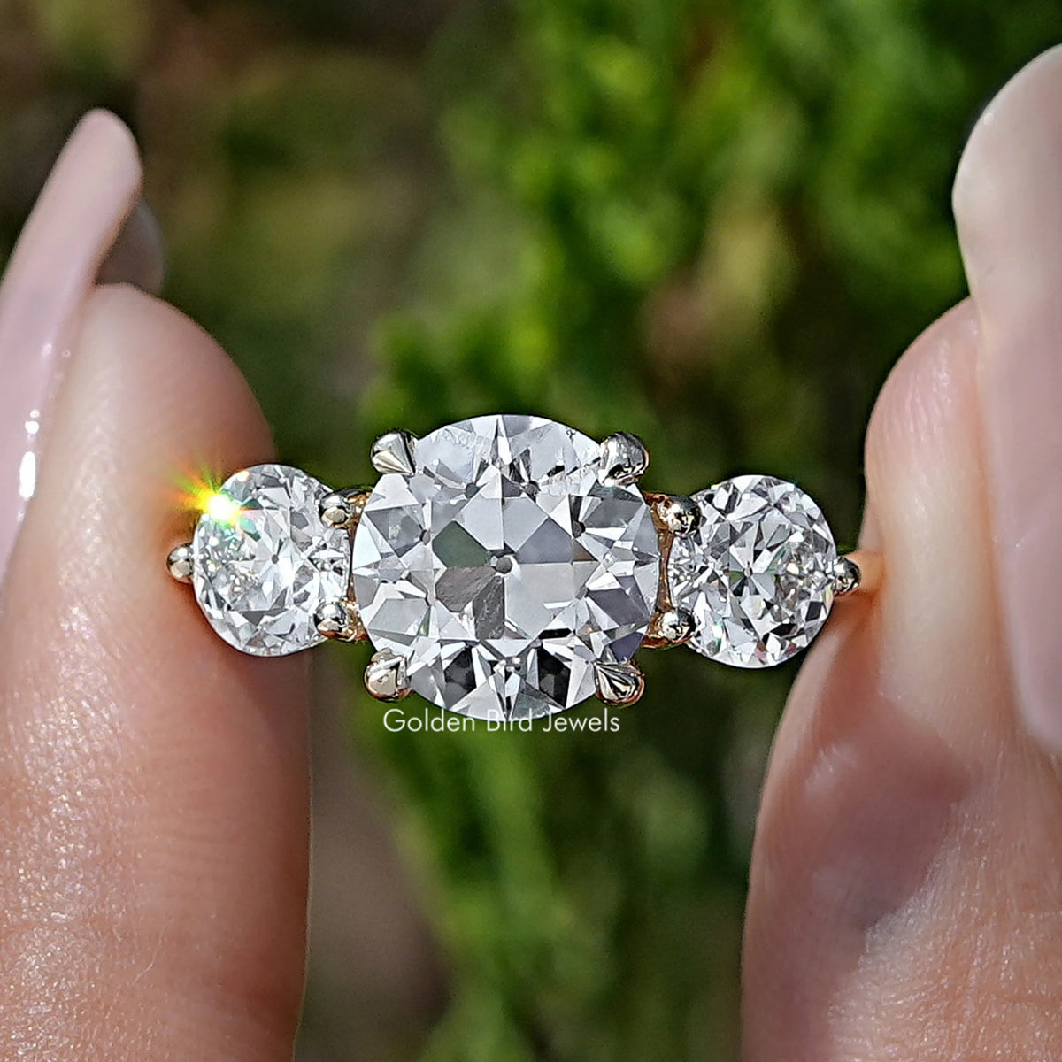 Old European Round Diamond Three Stone Ring Held Between Fingers