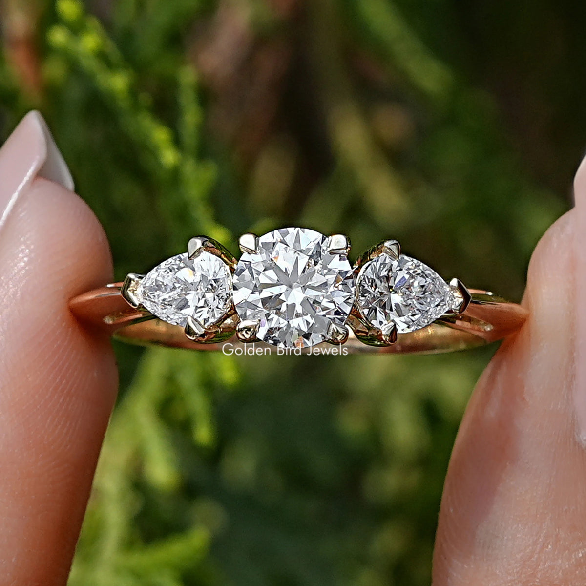 Pear and Round Cut Lab Diamond Three Stone Ring Held Between Fingers