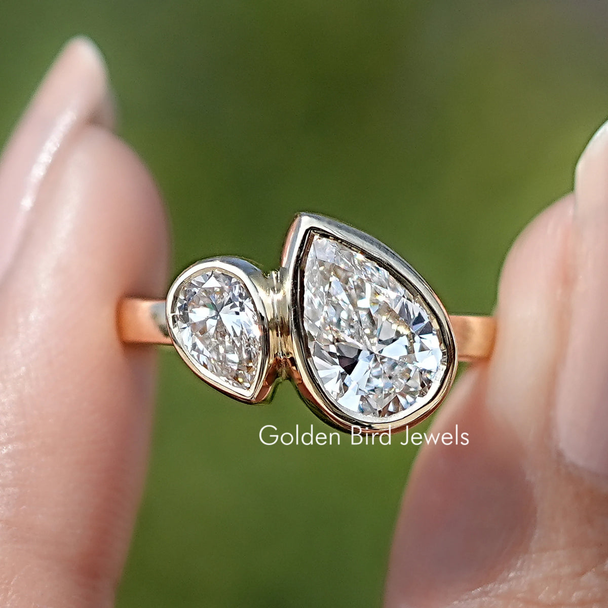 Bezel Set Pear Cut Lab Diamond Toi Et Moi Ring Held Between Fingers