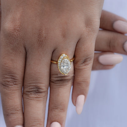 Gold oval moissanite halo ring worn on hand with prong-set center stone