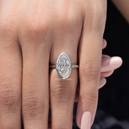 Close-up of oval bezel-set moissanite solitaire ring on finger, silver-toned band