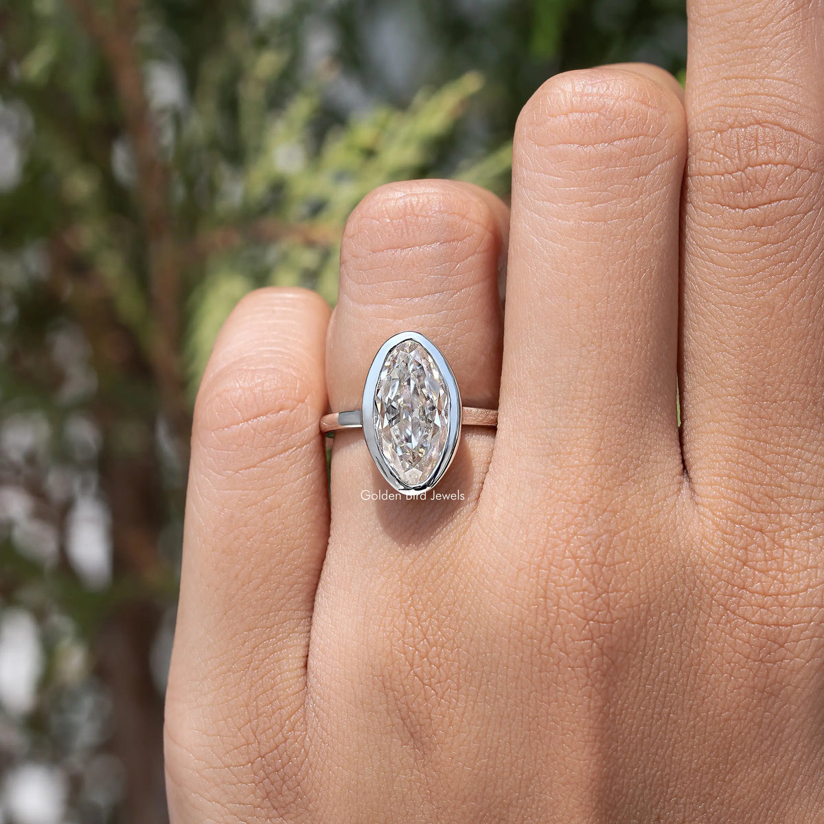 Oval bezel-set moissanite solitaire ring on hand, silver-toned band with slim shank
