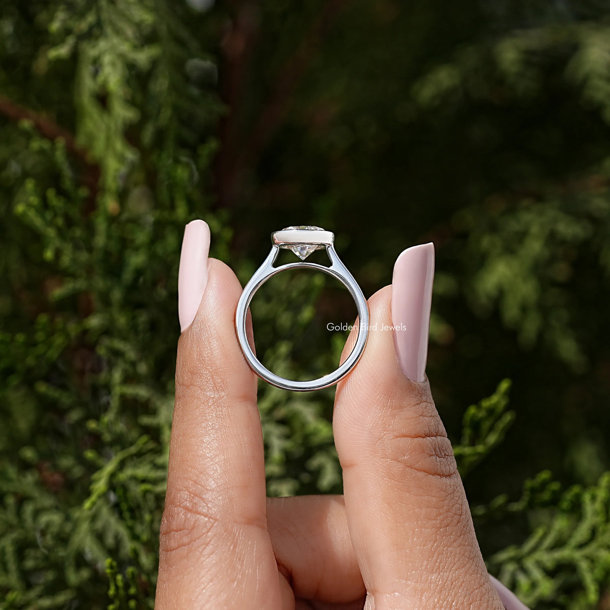 Sterling silver round moissanite bezel wedding ring, ring profile held between fingers