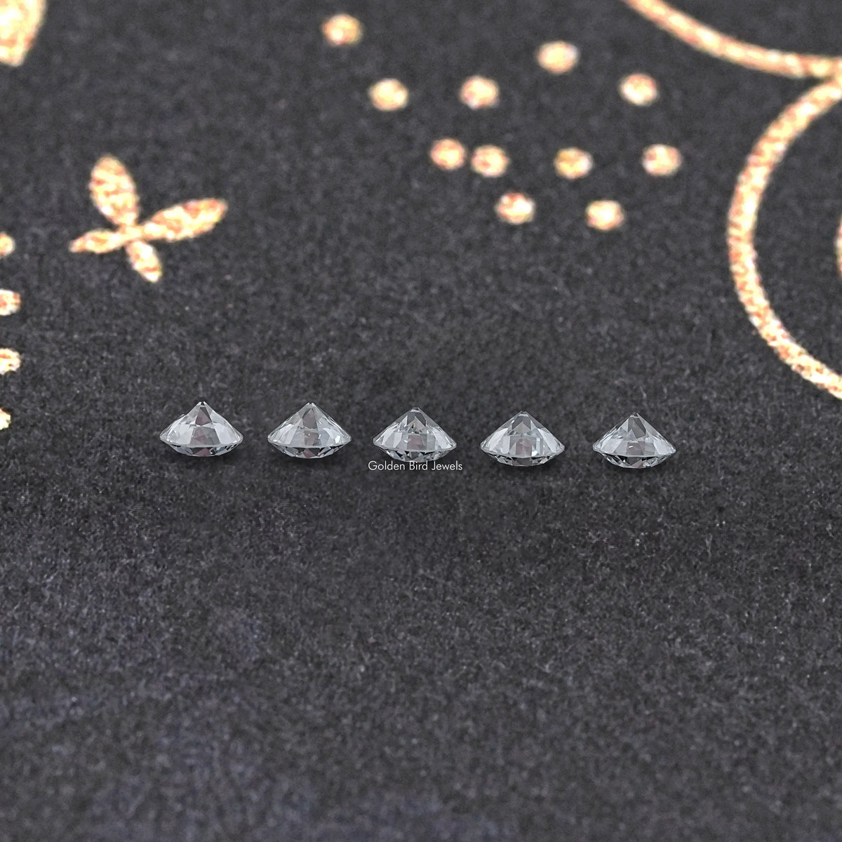 Set of five round lab-grown diamonds in prong settings on dark pad