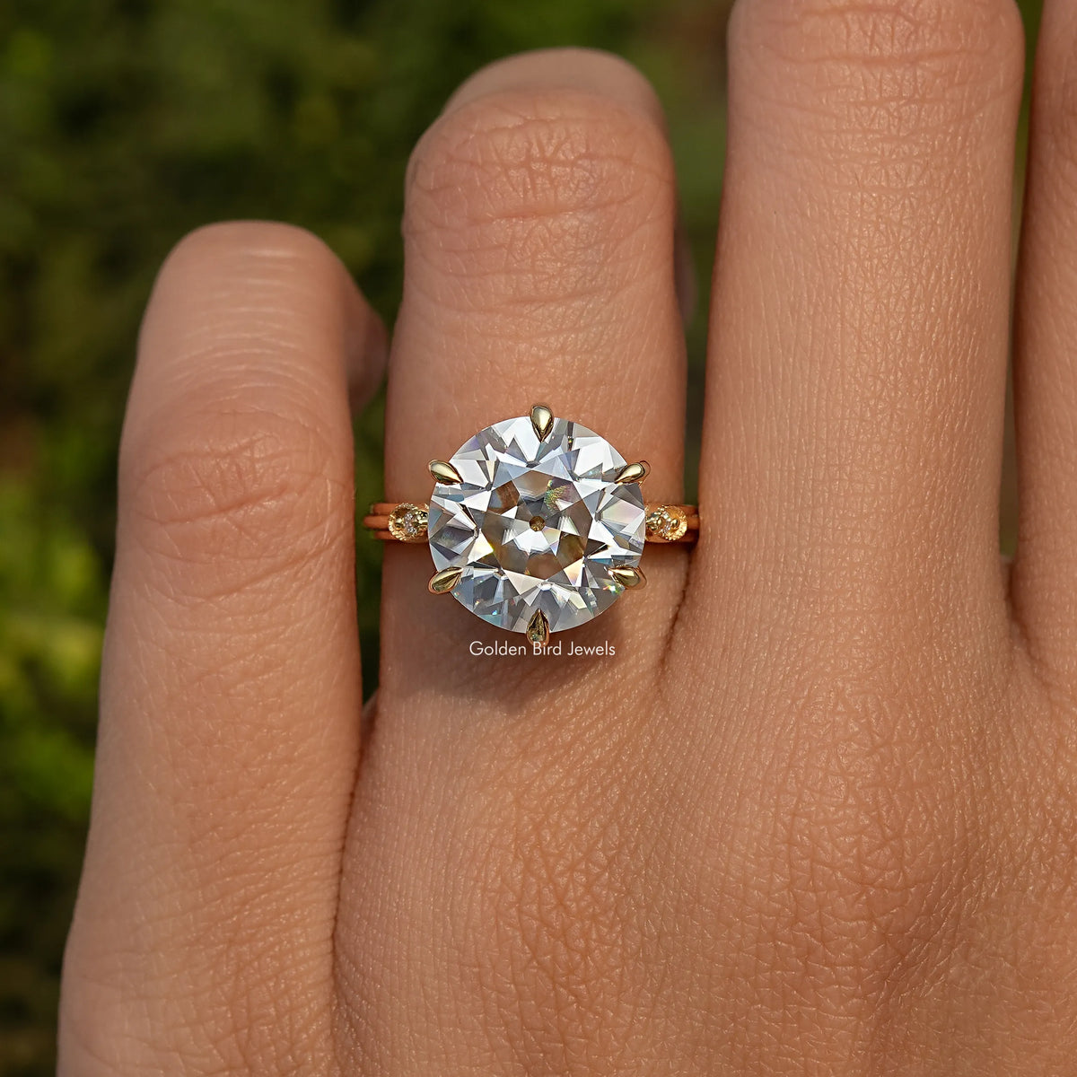 Round moissanite ring on finger, rose-gold tone band with small side stones