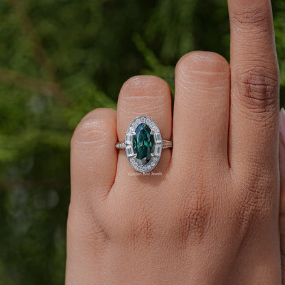 Oval halo ring with dark green center stone on a silver band, finger view