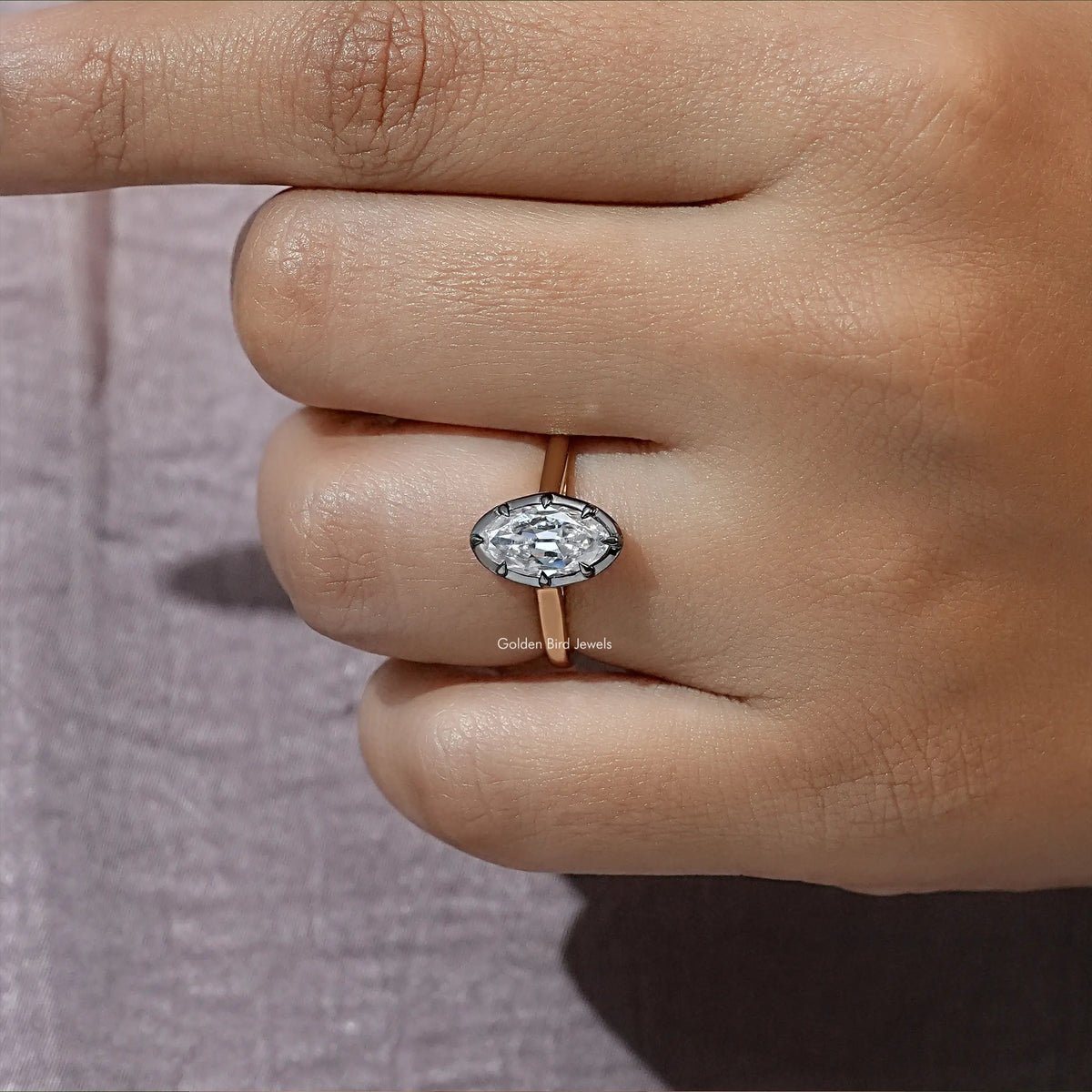 Oval moissanite bezel-set solitaire ring on gold-tone band, close-up on finger