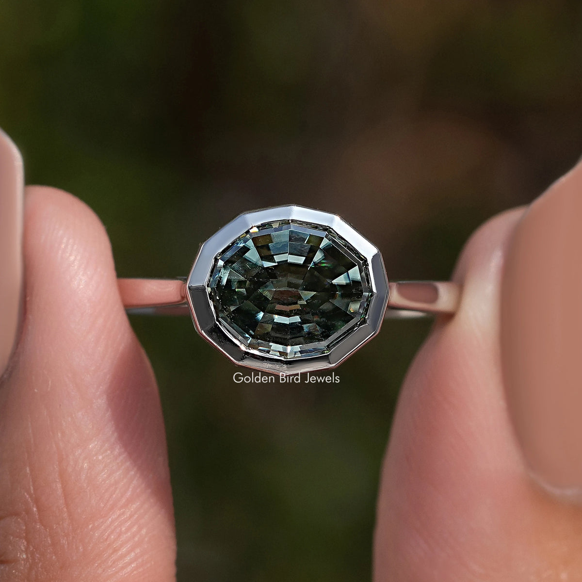 Close-up of dark green step-cut solitaire gemstone in polished silver bezel setting