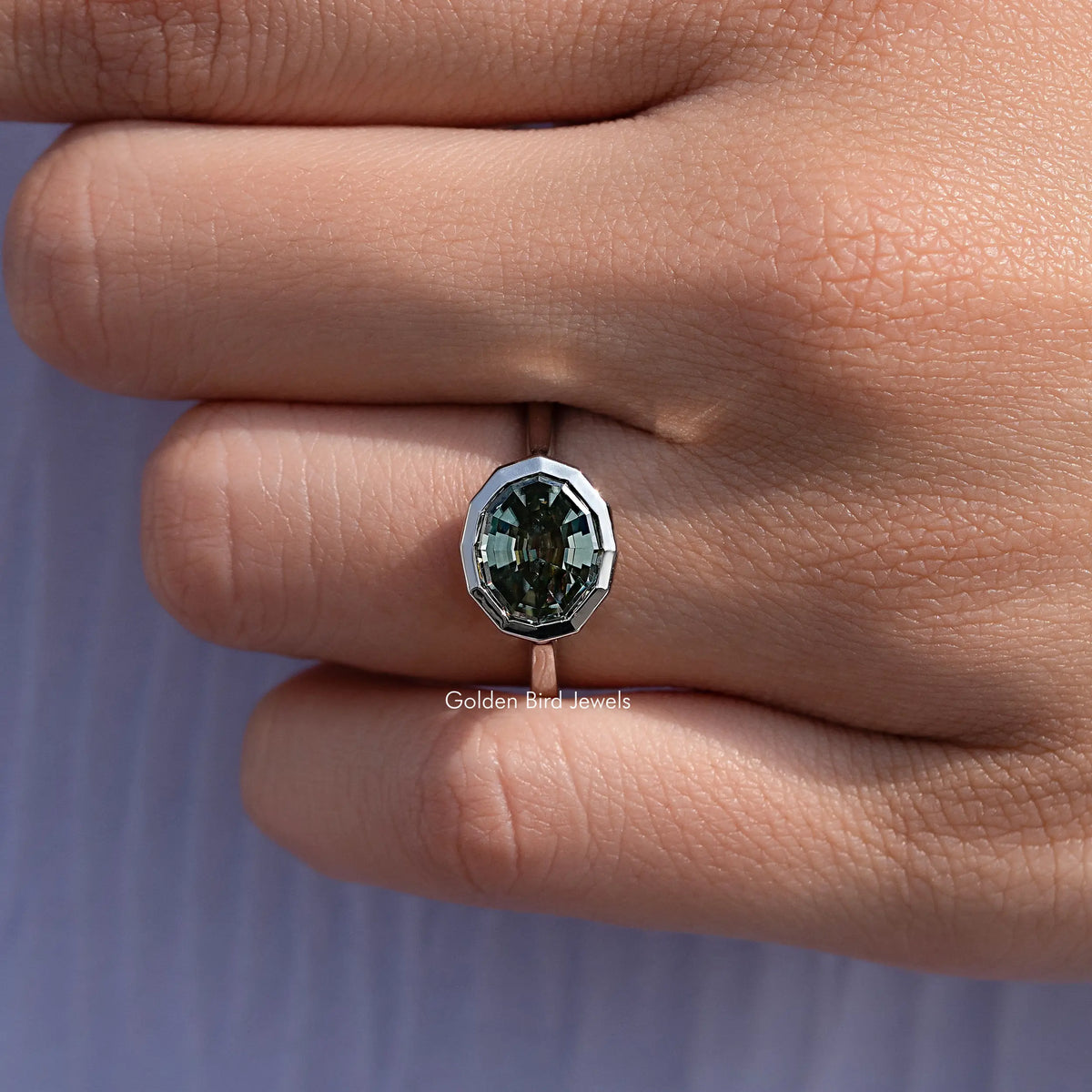 Dark green step-cut solitaire ring with polished silver bezel on finger