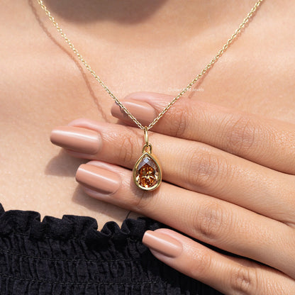Gold teardrop pendant necklace on hand, champagne pear-cut gemstone