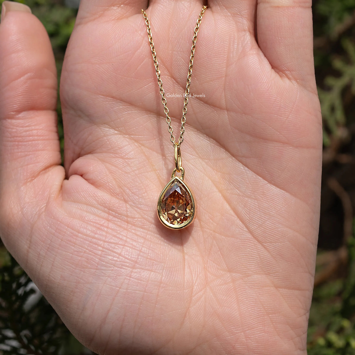 Gold teardrop pendant necklace shown in hand, champagne pear-cut gemstone