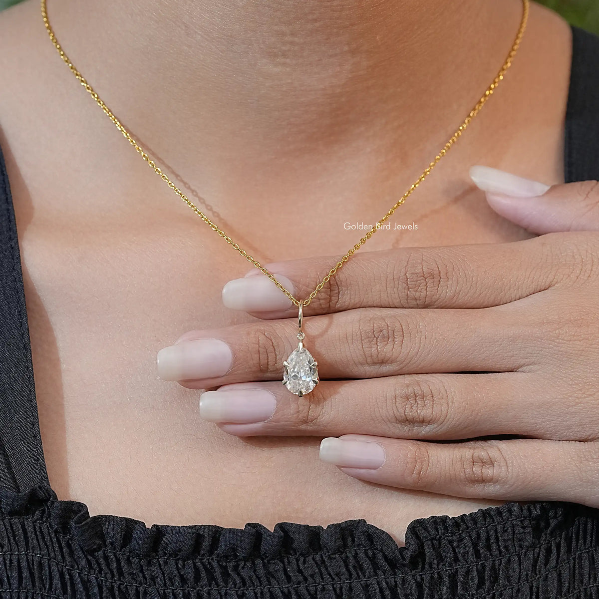 Hand holding gold-tone pear-cut moissanite solitaire pendant with teardrop stone